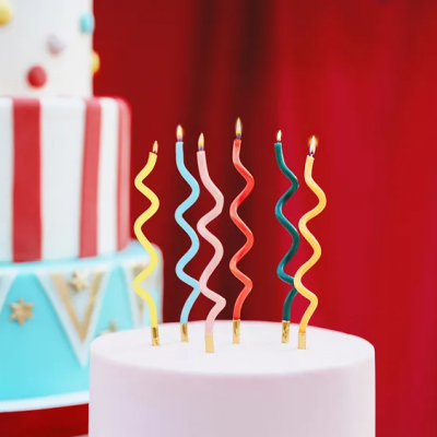Cinco velas onduladas acesas em bolo branco com bolos decorados ao fundo