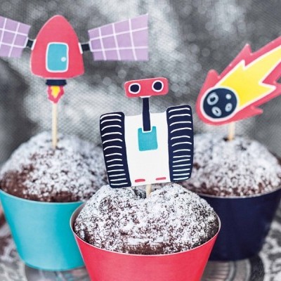 Três cupcakes com toppers de papel com tema espacial em copos coloridos sobre prato