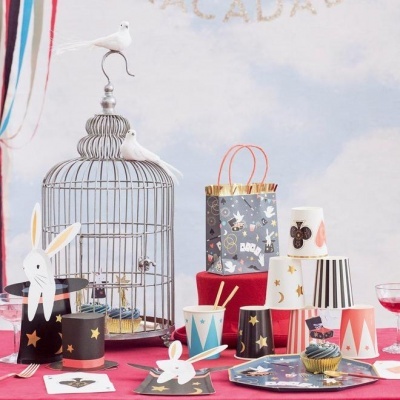 Mesa de festa com chapéus de papel, gaiola decorativa, sacos e cupcakes coloridos