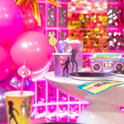 Copos e caixa de papel para festa com tema de discoteca em cores roxo, amarelo e preto, com balões rosas e dourados