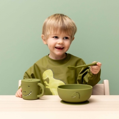 Conjunto de utensílios infantis verdes com temática de dinossauro em mesa de madeira clara