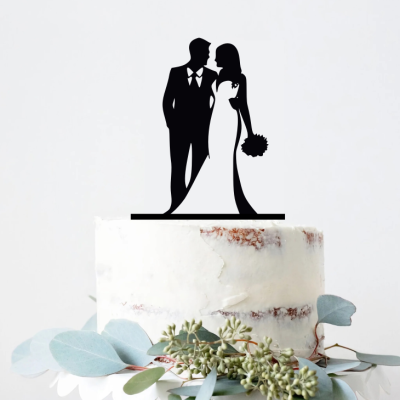 Topo de bolo de casamento com silhueta de casal em preto sobre bolo branco decorado com folhas verdes