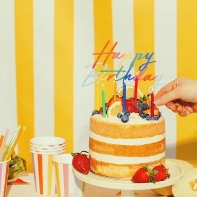 Bolo naked de aniversário com frutas frescas e velas coloridas numa mesa com copos e guardanapos listrados