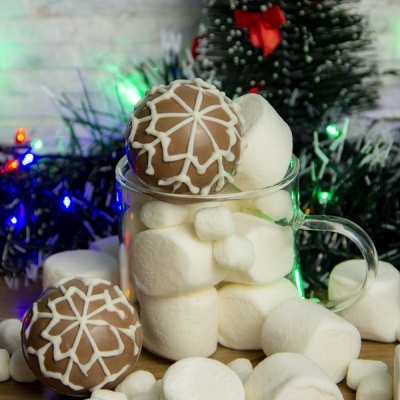 Caneca cheia de marshmallows brancos e bolachas de chocolate decoradas com glacê em padrão natalício.