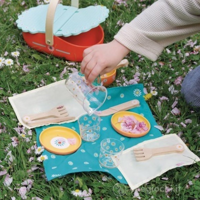 Conjunto de piquenique infantil colorido com pratos, copos e talheres sobre relva florida