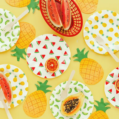 Pratos descartáveis com padrões de frutas, frutas frescas e cestos com snacks sobre fundo amarelo