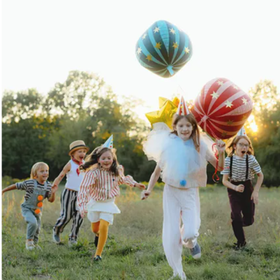 Crianças a correr num campo com balões de festa coloridos e chapéus de aniversário