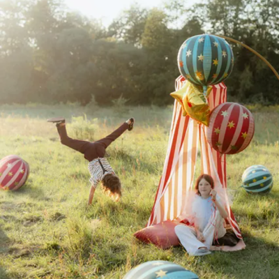 Tenda listrada e bolas coloridas com estrelas no relvado com crianças ao ar livre