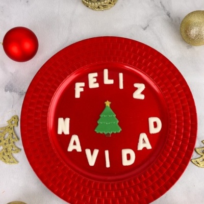 Prato vermelho com letras FELIZ NAVIDAD e árvore de Natal com bolas e enfeites natalícios