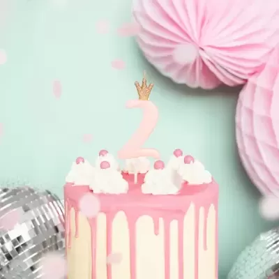 Bolo de aniversário decorado com vela número 2 em fundo com decoração rosa e bolas prateadas