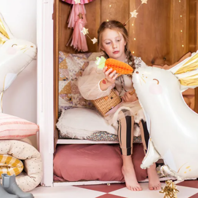 Criança a brincar numa pequena cama rodeada por balões infláveis em forma de coelho e almofadas coloridas