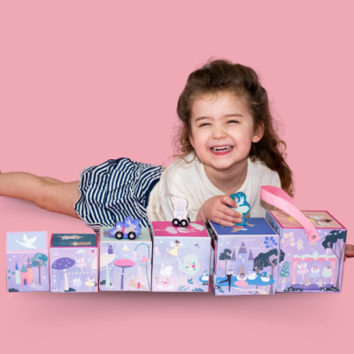 Criança sorridente com brinquedos e caixas coloridas em fundo rosa