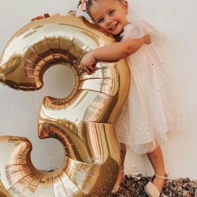 Menina com vestido branco a abraçar balão dourado número 3