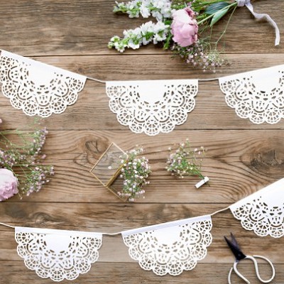 Guirlanda decorativa em papel branco recortado com flores e tesoura sobre madeira rústica