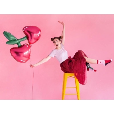 Mulher com saia vermelha segurando balão em forma de cerejas cor-de-rosa