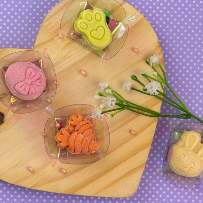 Quatro sabonetes decorativos em tamanhos e cores diferentes sobre tábua de madeira em forma de coração