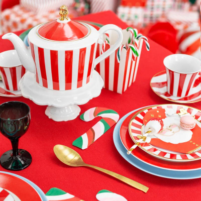 Mesa festiva com bule, chávenas e pratos com riscas vermelhas e decoração de Natal