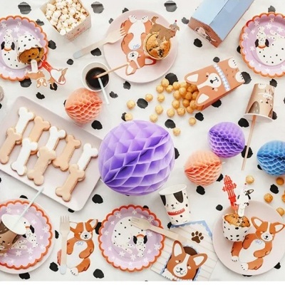 Mesa decorada com artigos de festa de tema cão, incluindo pratos, copos, caixas de pipoca e decorações de papel coloridas.
