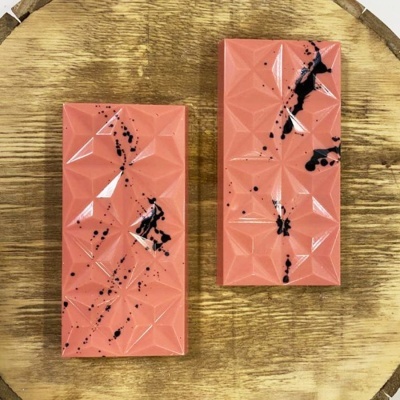 Barras de chocolate cor de rosa com padrão geométrico e manchas pretas sobre superfície de madeira