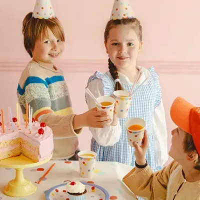 Crianças em festa de aniversário com bolo rosa e copos coloridos