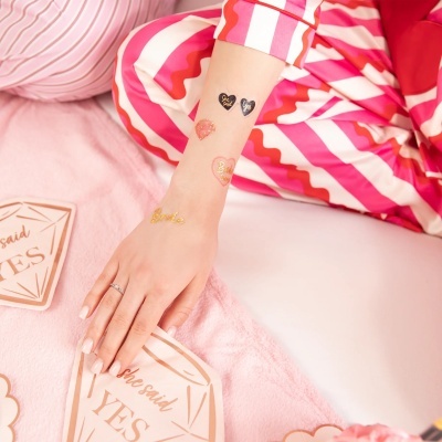 Braço com tatuagens temporárias douradas e pretas e pijama colorido às riscas.