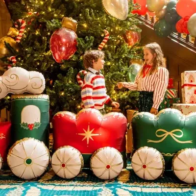 Tren inflável decorativo de Natal em vermelho, verde, branco e dourado junto a crianças e árvore de Natal