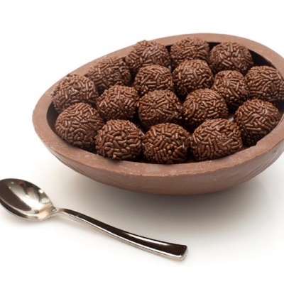 Ovo de chocolate com brigadeiros e colher em fundo branco