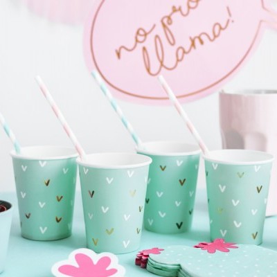 Copos de papel azul celeste com padrão de 'v' e canudos, vasos com plantas e decoração colorida numa mesa azul clara.