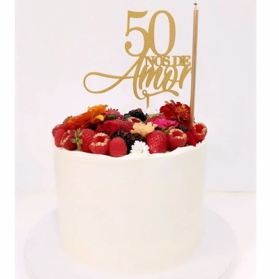 Bolo decorado com frutas vermelhas, flores e placa dourada com texto '50 ANOS DE AMOR'