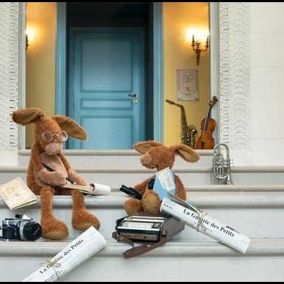 Duas peluches coelho castanho com acessórios em escadas brancas e porta azul ao fundo