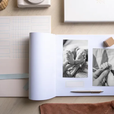 Livro de memórias aberto com fotos de bebé e caneta sobre mesa de madeira clara