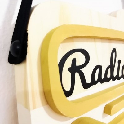 Placa decorativa em madeira clara com texto 'Radio' e relevo amarelo