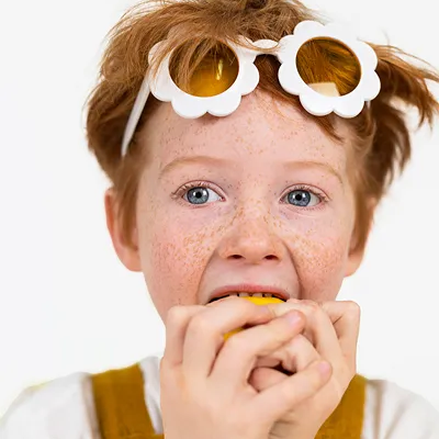 Criança ruiva com óculos de sol florais a morder fruta