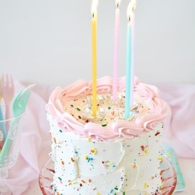 Bolo de aniversário branco e rosa com velas coloridas acesas