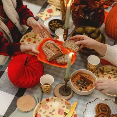 Mesa de refeições outonal com pratos decorados, pão, velas e decoração natural