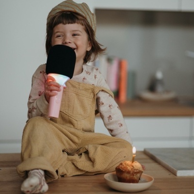 Criança com microfone de brinquedo e cupcake com vela sentada numa bancada de madeira