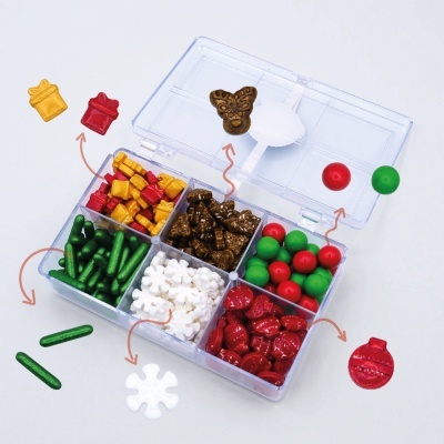 Caixa transparente com compartimentos contendo miniaturas de presentes, flocos de neve, bolas e outros enfeites coloridos para decoração.