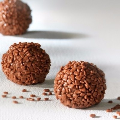Três brigadeiros de chocolate com granulados sobre superfície branca