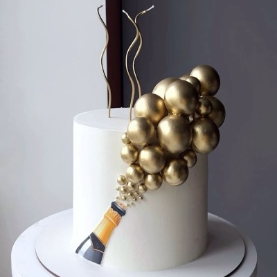 Bolo branco decorado com garrafa de champanhe e bolhas douradas em relevo