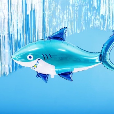 Balão em forma de tubarão azul contra fundo azul claro e cortinas metálicas prateadas