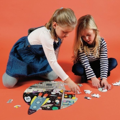 Duas meninas montando um puzzle colorido de foguetão no chão laranja