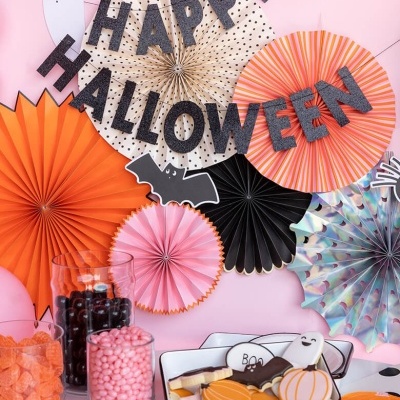 Decoração colorida de Halloween com painéis de papel, letras e doces em recipientes e uma travessa com bolachas decoradas