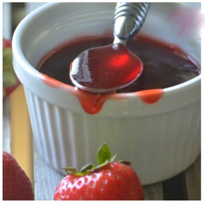 Frasco branco de cerâmica com geleia vermelha e colher, morango vermelho ao lado