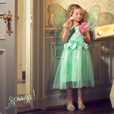 Menina com vestido de fada verde e asas transparentes segurando espelho e escova de cabelo em interior clássico