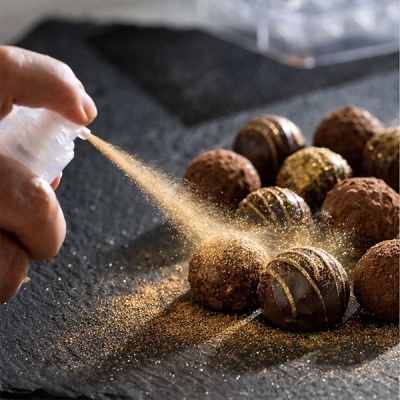 Trufas de chocolate polvilhadas com spray dourado sobre superfície preta