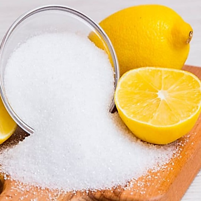 Sal grosso branco derramado de concha metálica ao lado de limões amarelos em tábua de madeira