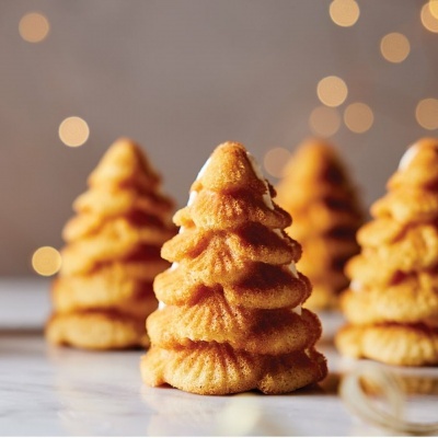 Bolos em formato de árvore de Natal dourados sobre superfície branca com luzes desfocadas ao fundo