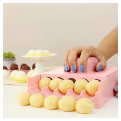 Aparelho rosa para moldar bolinhas de massa com bolinhas amarelas e mão segurando