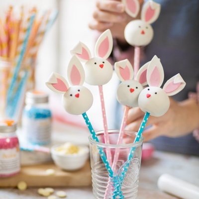 Cake pops decorados como coelhos de Páscoa em palitos dentro de copo de vidro na cozinha