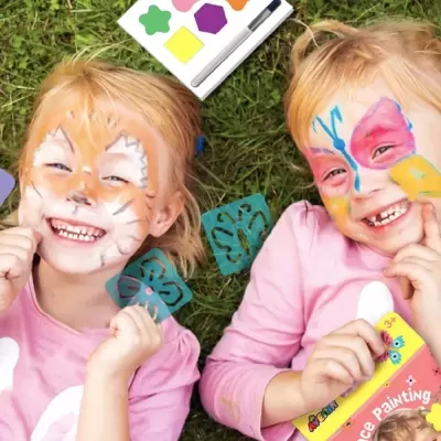Crianças com pintura facial de gato e borboleta, deitadas na relva com stencil de borboleta e embalagem de pintura facial.